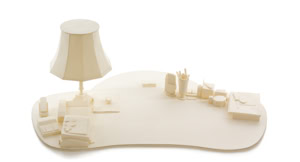 Precise three-dimensional paper reconstruction of a workspace by Herbert Stattler, showing desk objects as monochromatic white paper models based on original pencil drawings.