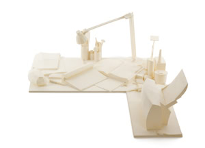 Precise three-dimensional paper reconstruction of a workspace by Herbert Stattler, showing desk objects as monochromatic white paper models based on original pencil drawings.